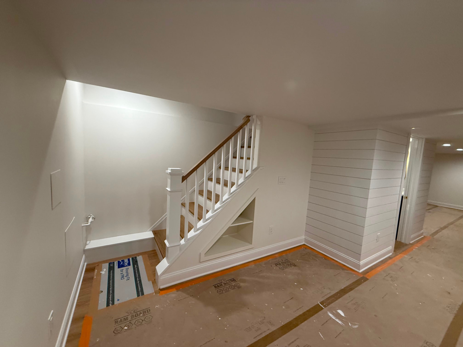 Painted basement stair with white balusters, newel post and built-in shelf under the stair