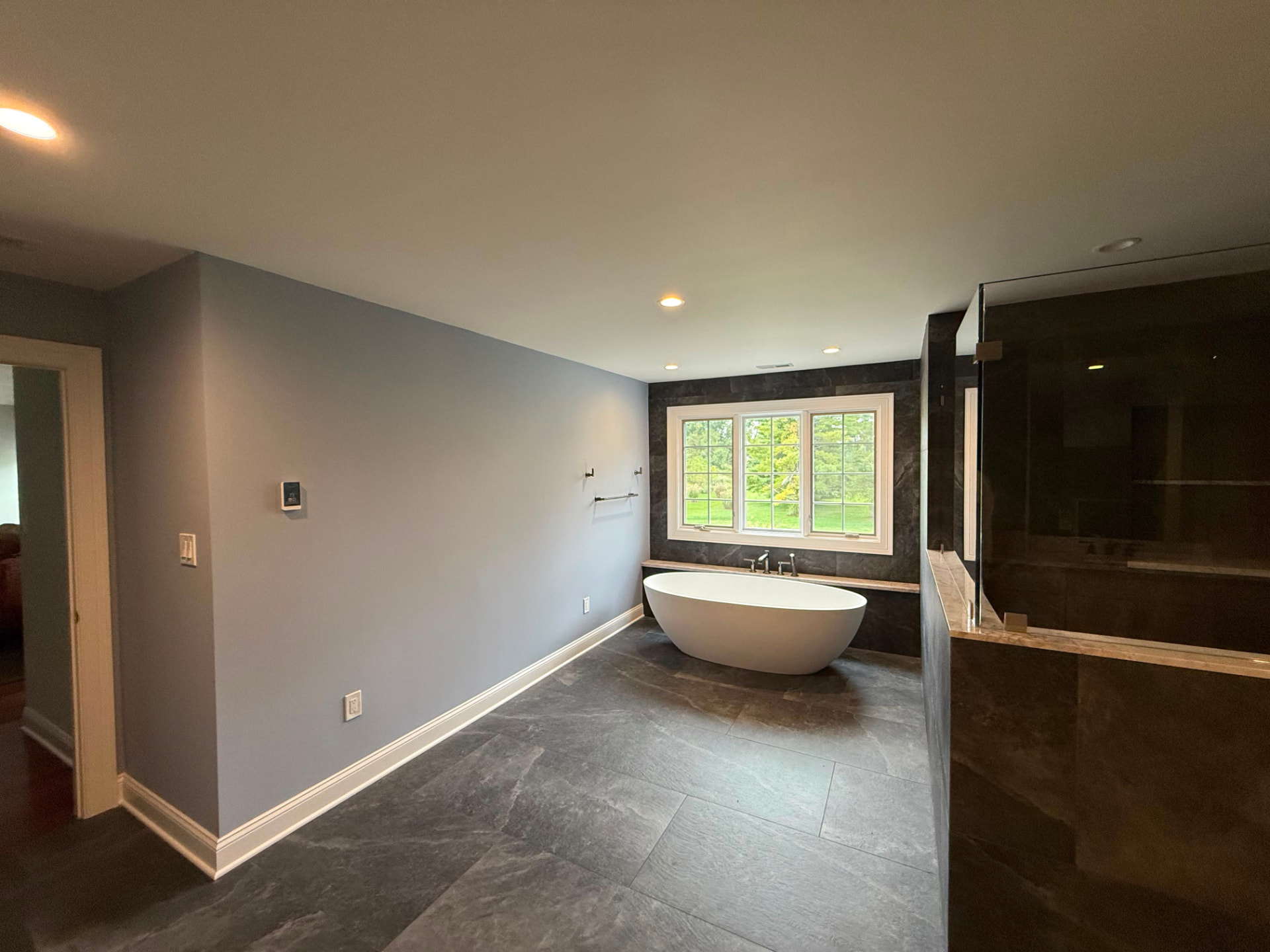 Freestanding tub under a window with blue-gray walls and white baseboard
