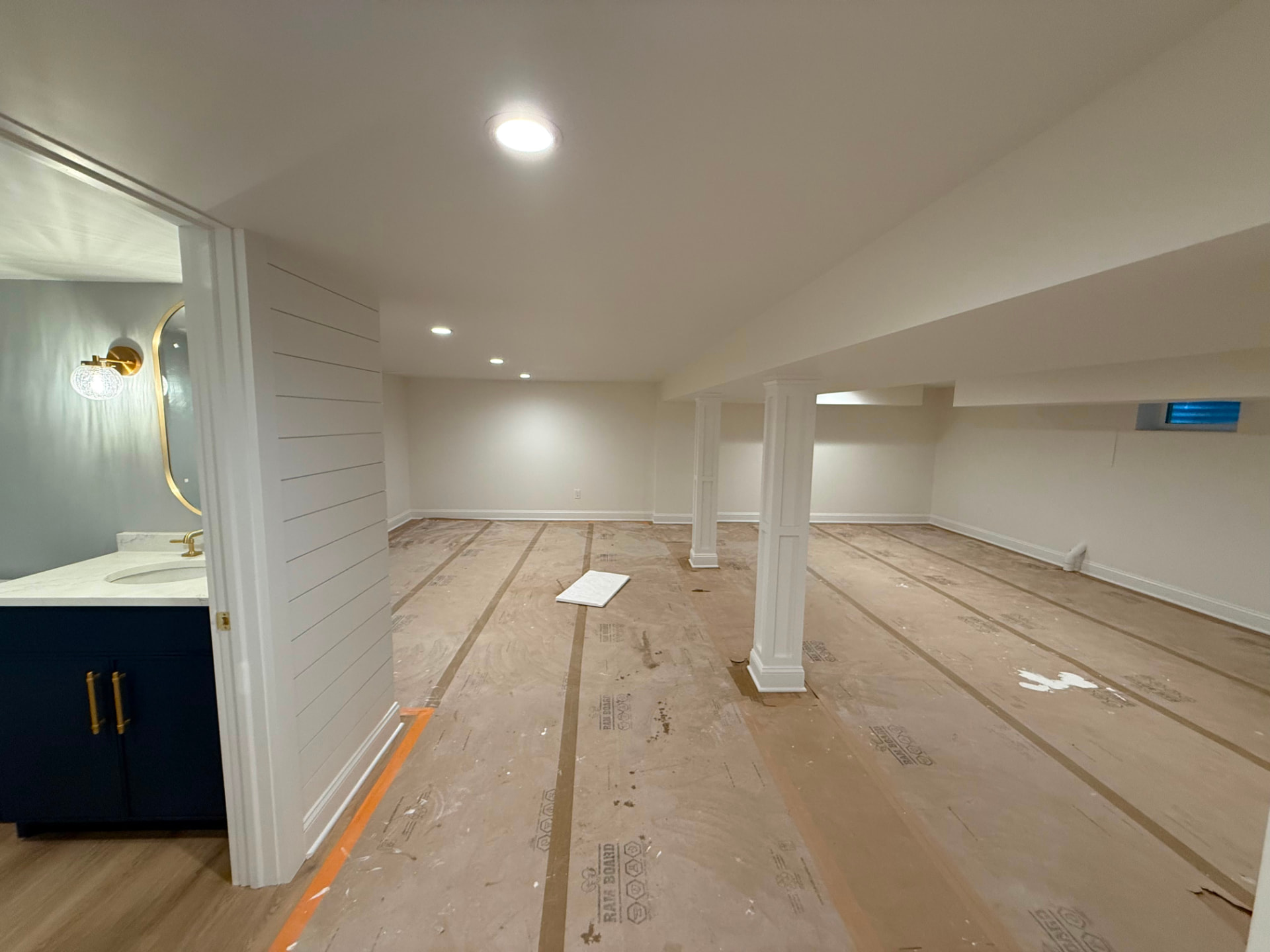 Long painted basement with wrapped columns and the powder room doorway