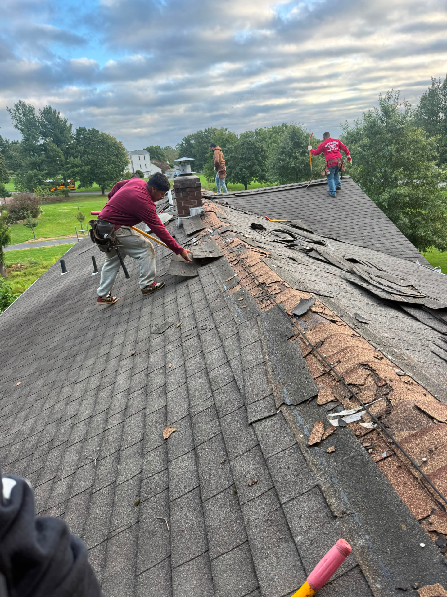 Roofing crew tearing off old worn asphalt shingles along a roof ridge