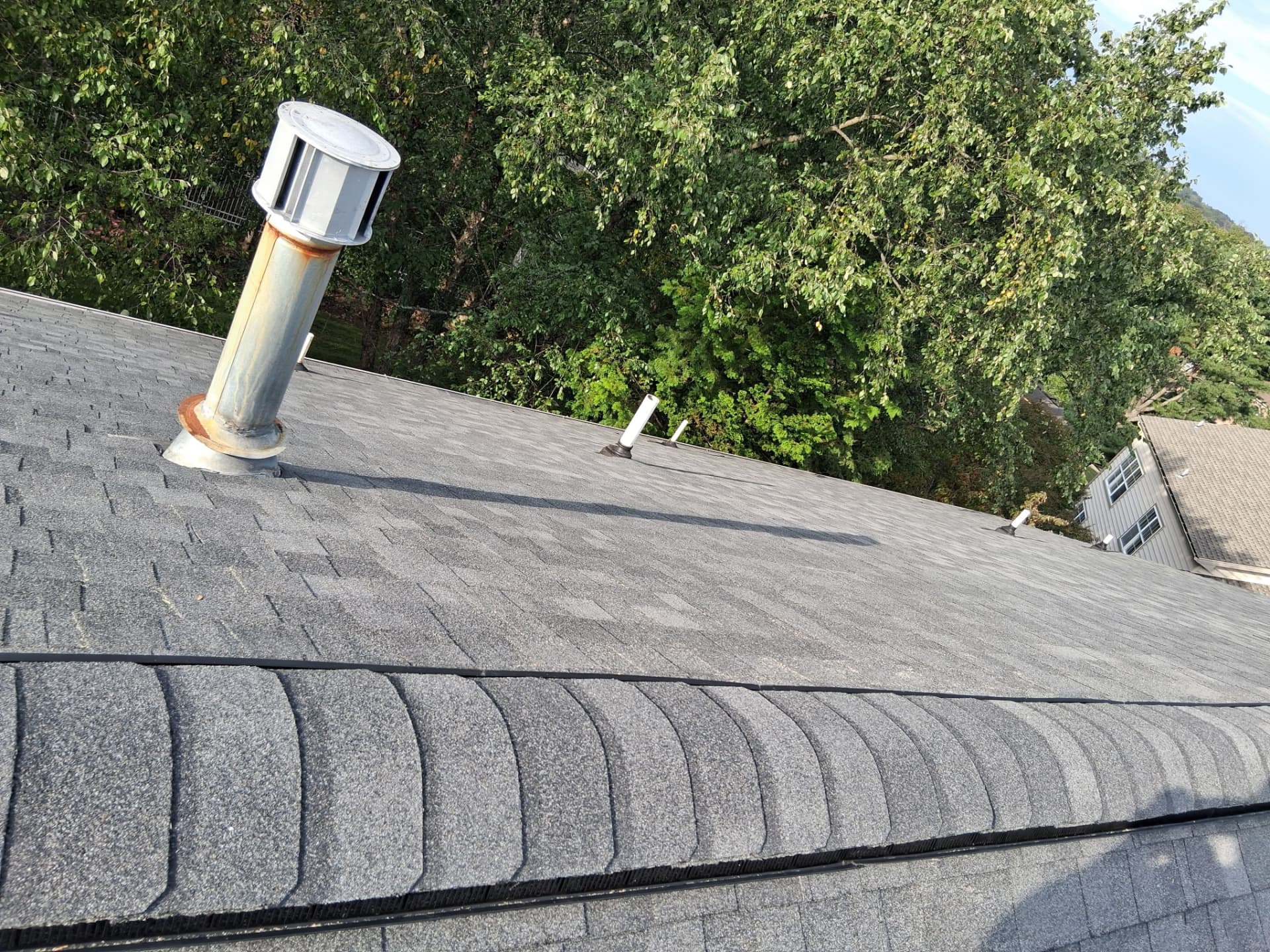 Finished gray shingle roof with ridge vent, plumbing boots and a metal exhaust vent