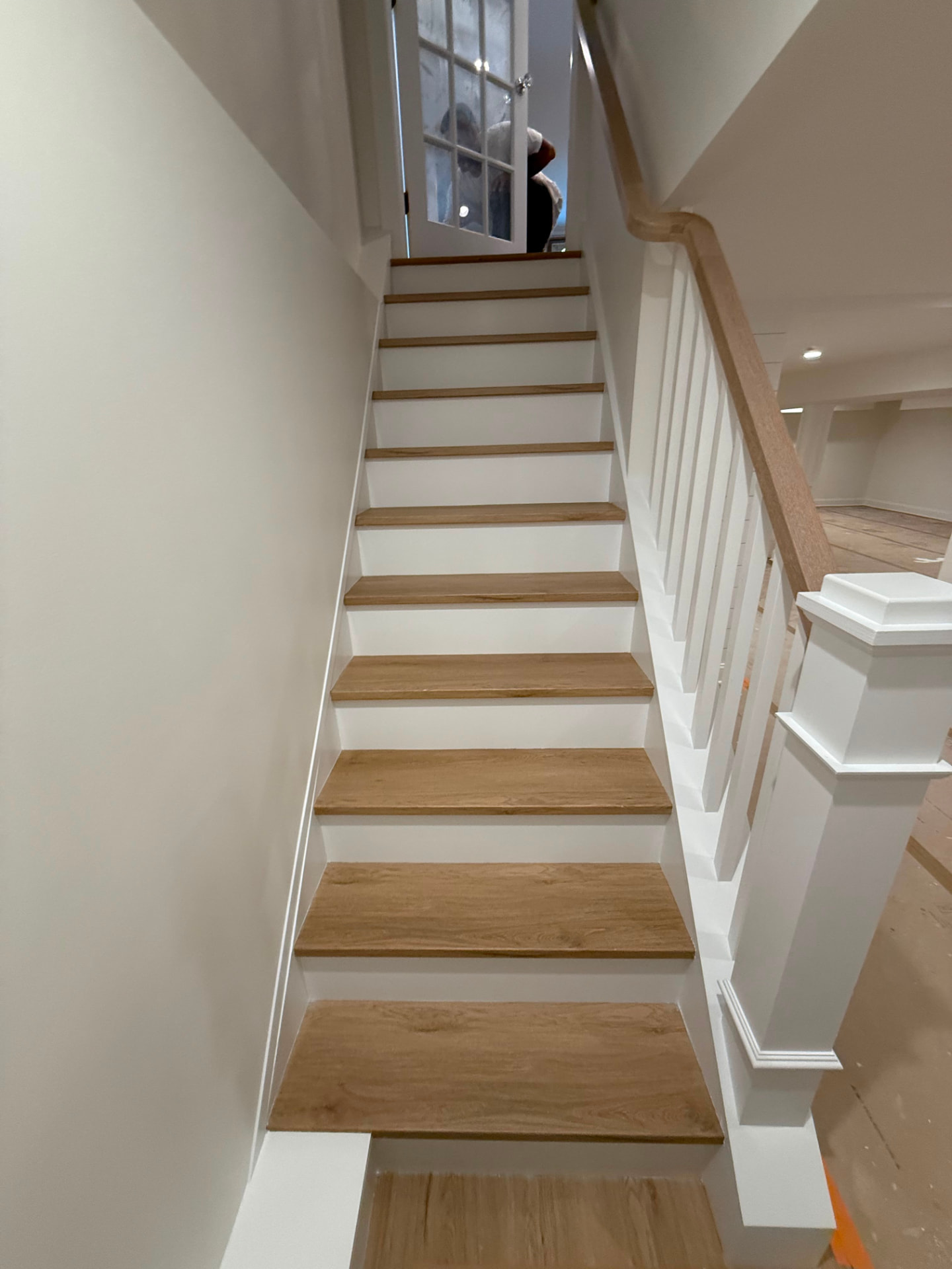 Basement staircase with white risers and balusters below a natural wood handrail