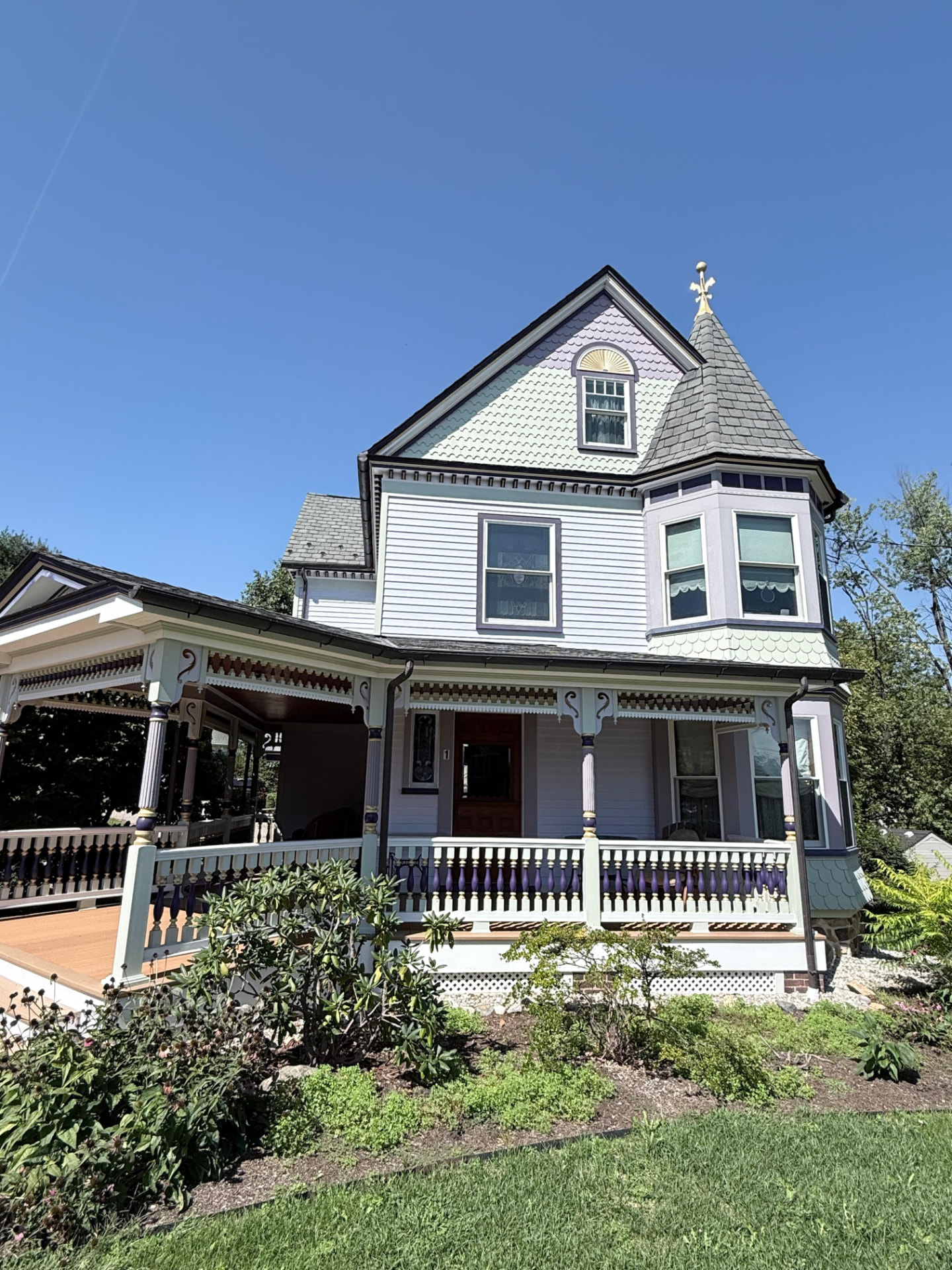 Painted Victorian front with a fish-scale gable, gold sunburst and spindle porch