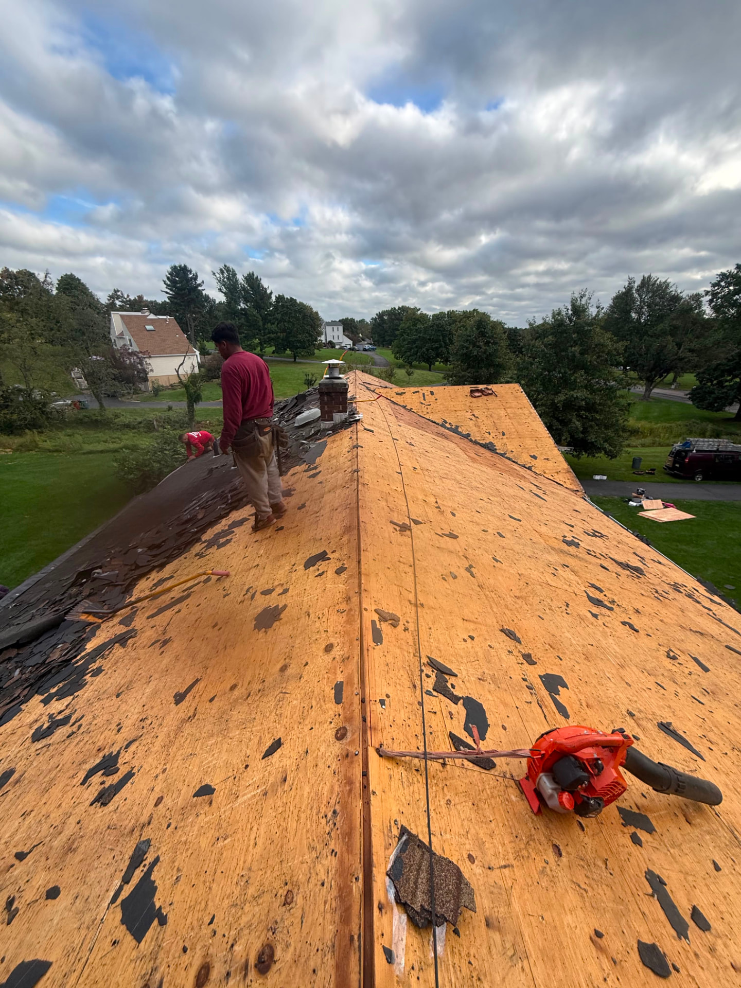 Roof stripped to bare plywood decking with a roofer inspecting the surface