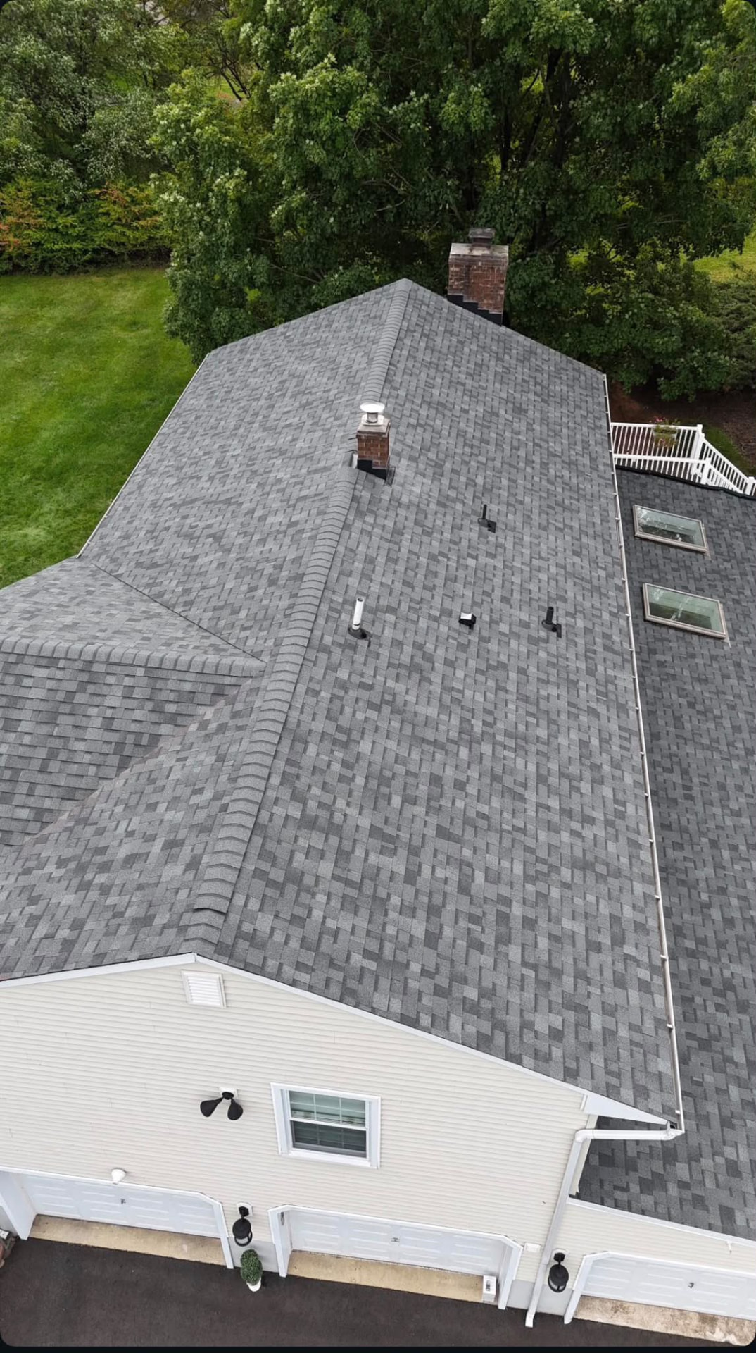 Aerial view of a completed gray architectural shingle roof with ridge caps, skylights and white gutters