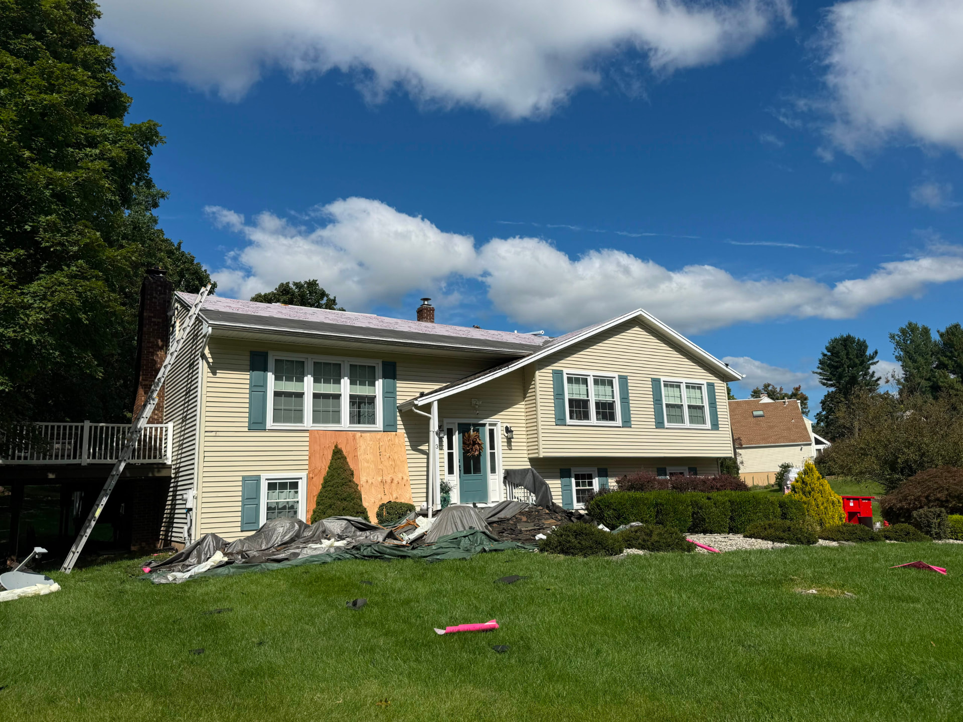 Split-level home mid roof replacement with tarps protecting the landscaping