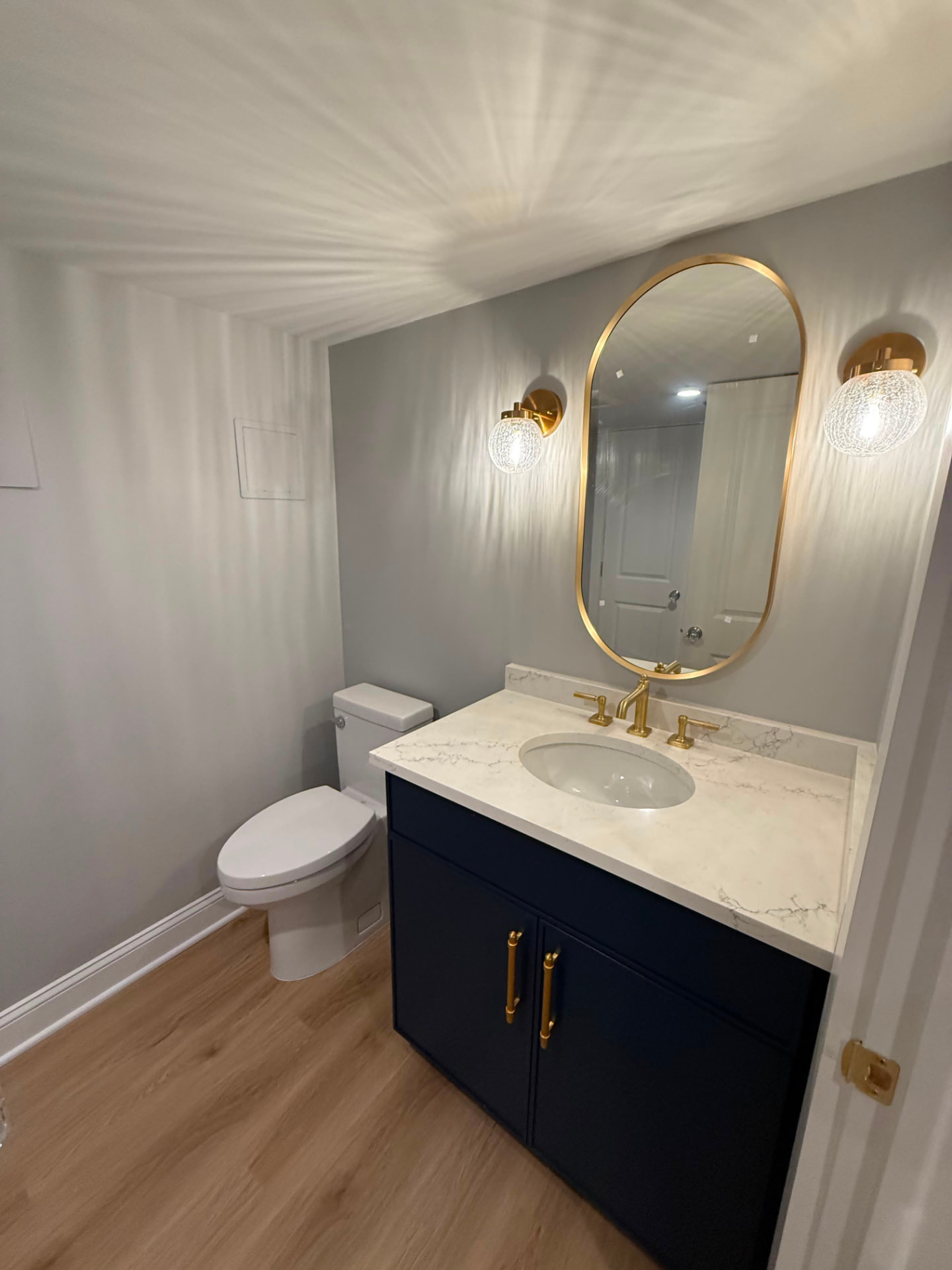 Powder room with soft grey walls, navy vanity, brass mirror and globe sconces