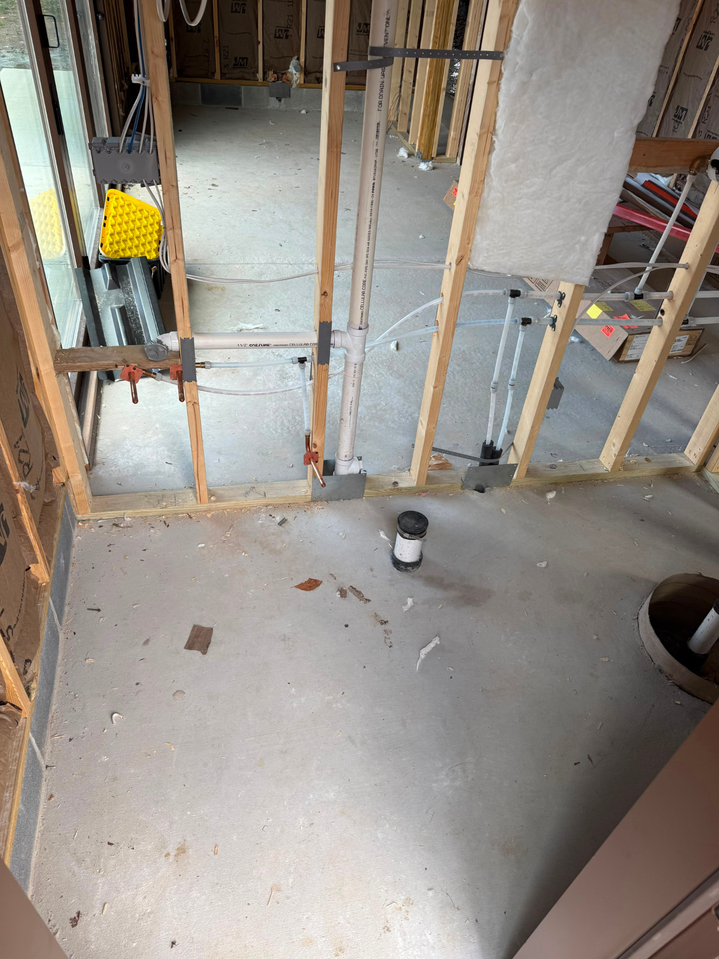 Bathroom area with open stud walls, drain and supply lines on bare concrete
