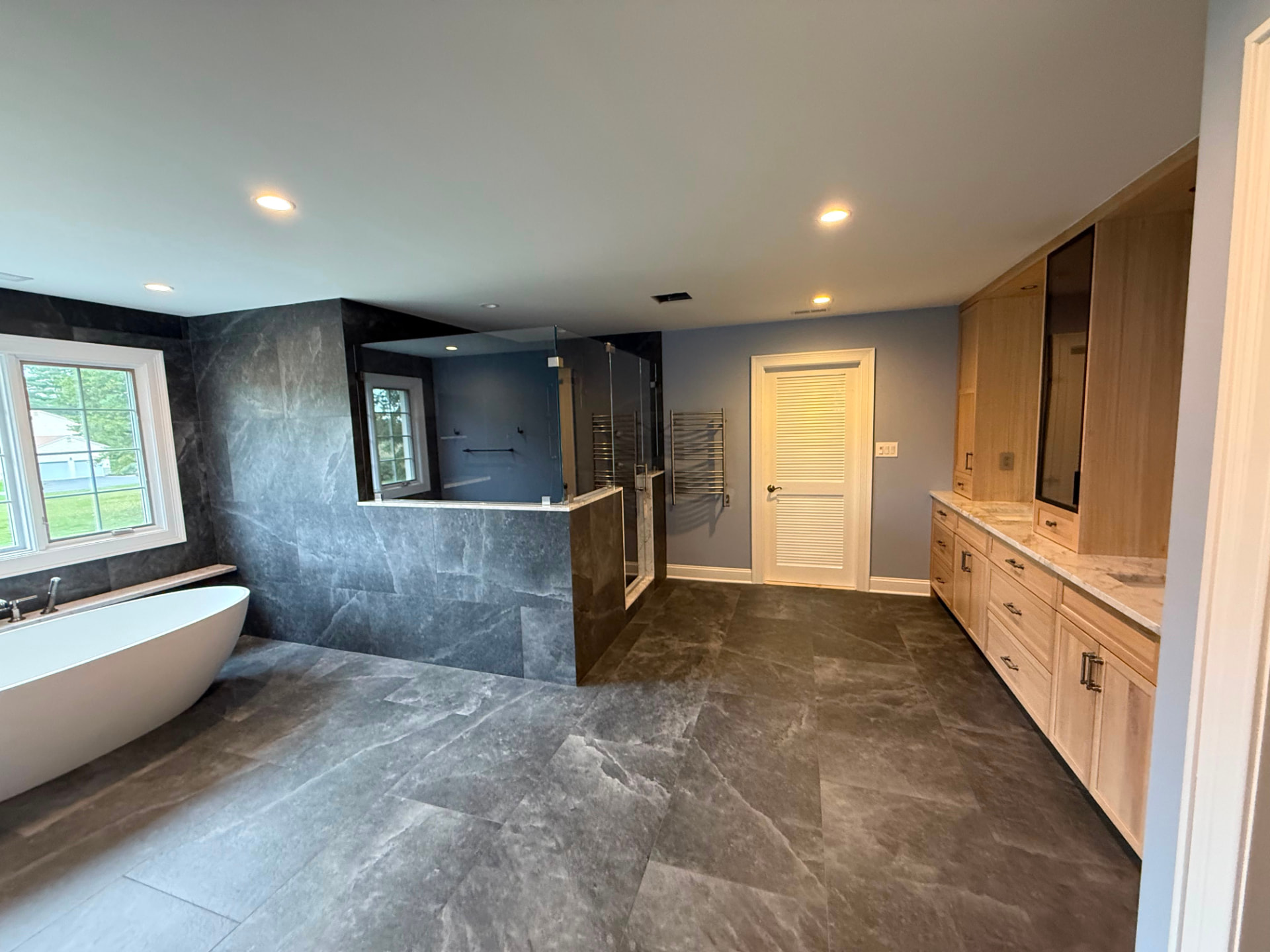 Primary bathroom in Flemington, NJ with blue-gray walls, freestanding tub, glass shower and wood vanity