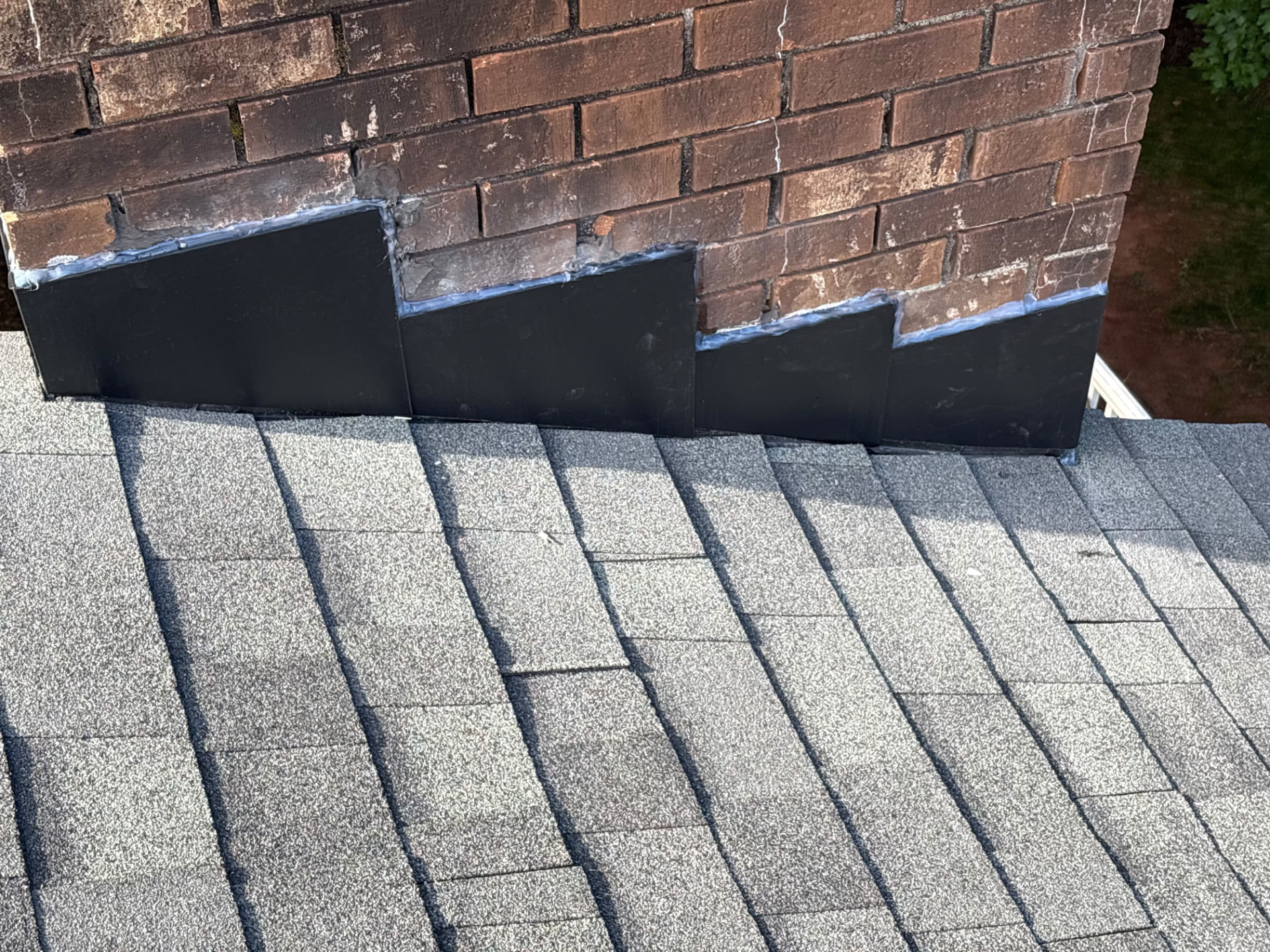 New black step flashing sealed around a brick chimney on a shingle roof