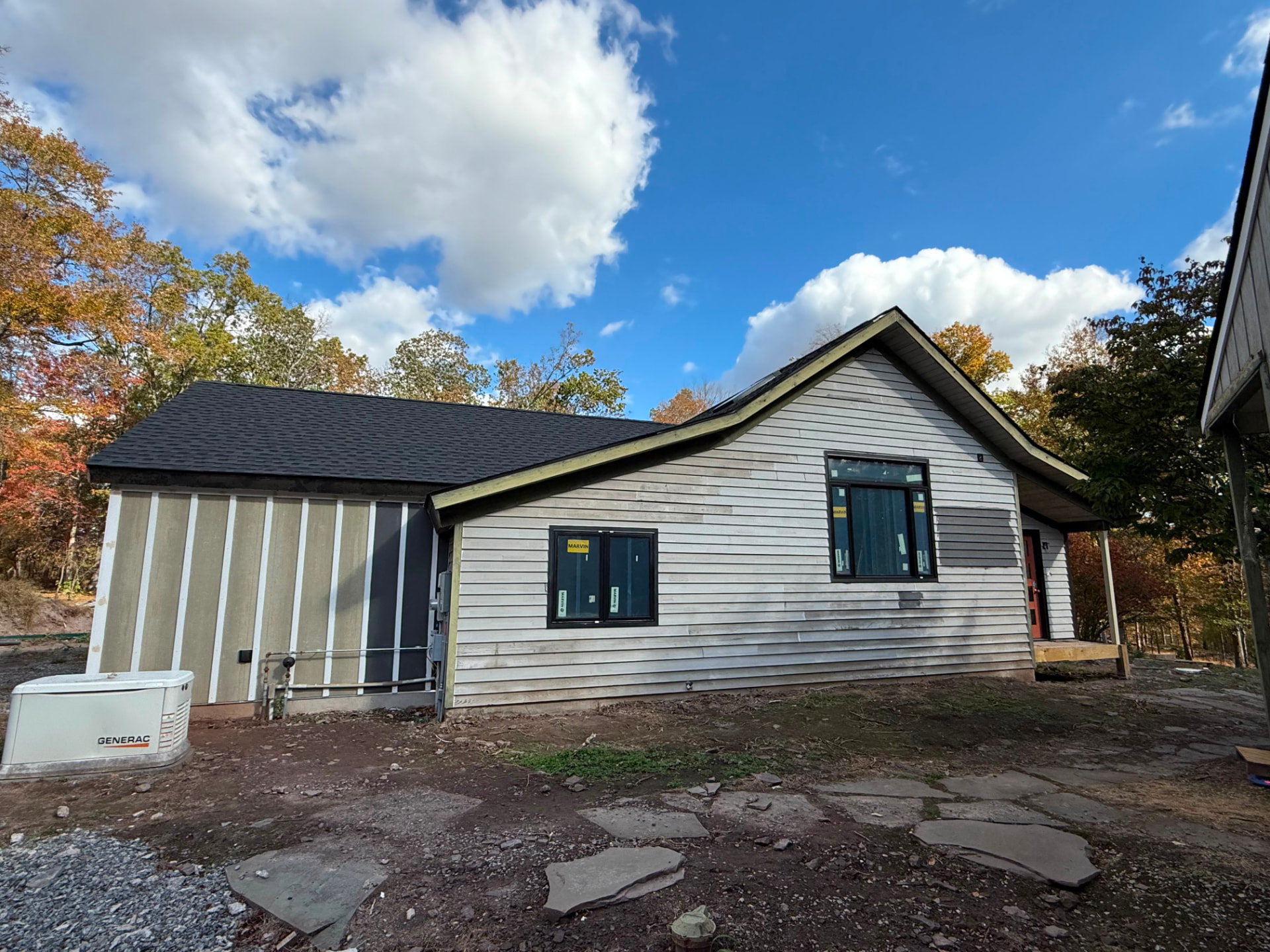 Side of the home with pale lap siding and a dark color sample patch