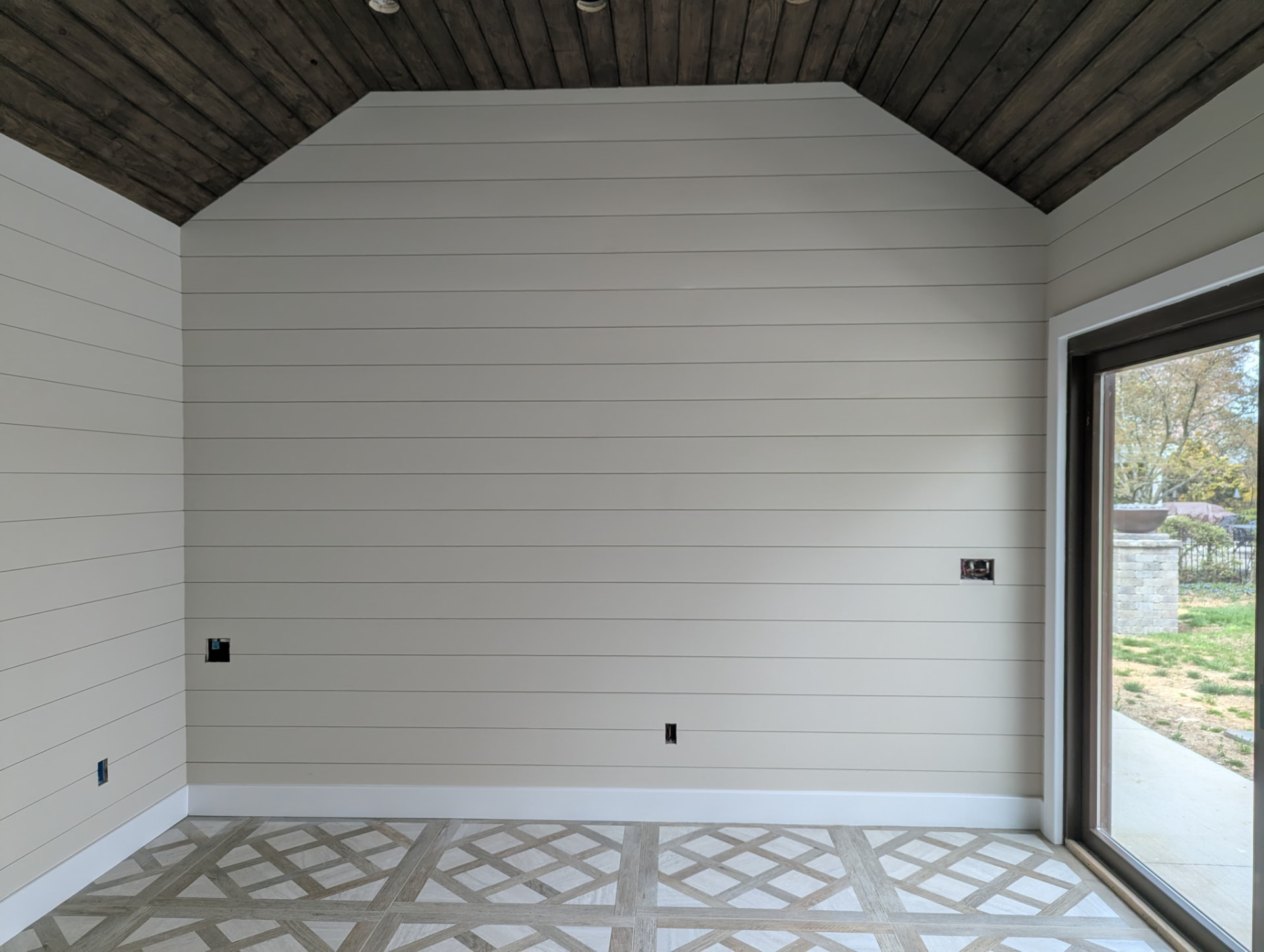 Painted shiplap gable wall with white baseboard and patterned tile floor