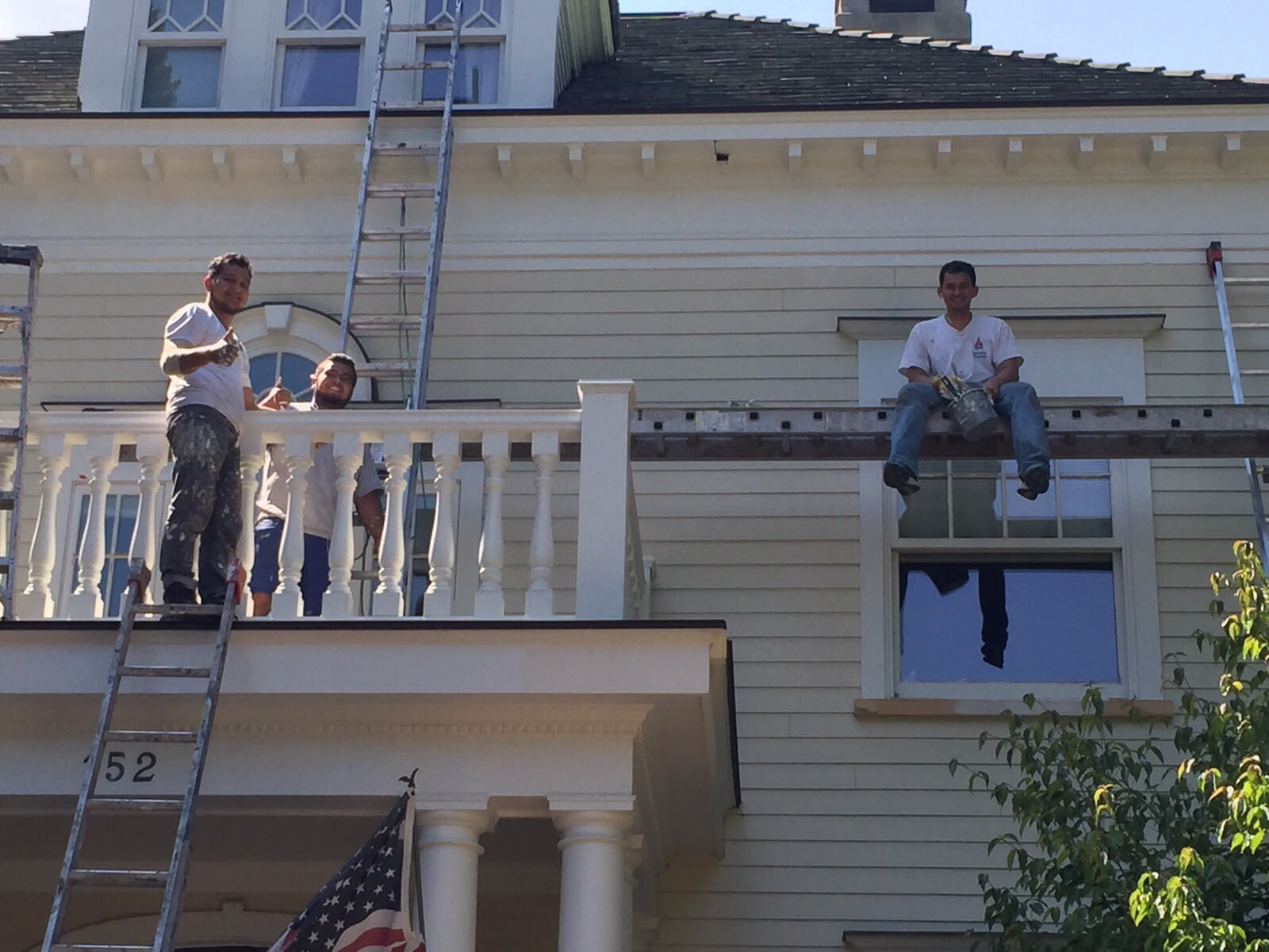 Painters on a balcony and ladder painting porch trim and balusters on a light-sided home